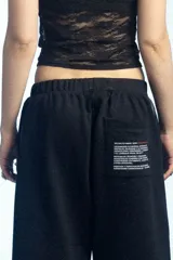 Bermuda deportiva de felpa color negro, de corte ancho y largo por debajo de las rodillas, con cintura elástica.