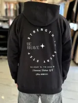 Canguro oversize marrón con capucha, bolsillo tipo canguro y diseño estampado en la espalda con el texto "Be Brave" y detalles tipográficos en color blanco.