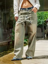 Pantalón de jean de lavado claro (oxido), corte ancho y tiro bajo, con cordones ajustables a la vista en la cintura y bordado en el frente.
