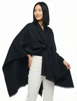 Ruana de tejido soft color negro, con cuello en V y un nudo o pasador frontal que ajusta la prenda. Los bordes tienen terminación desflecada.