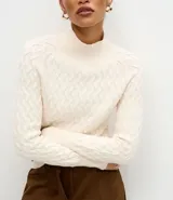 Suéter de punto color crema con textura en zigzag, cuello alto y mangas largas con puños ajustados.