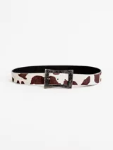 Cinto de cuero con estampado tipo animal print de vaca en tonos marrón y blanco, con hebilla metálica rectangular envejecida.