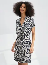 Vestido corto con estampado animal print tipo cebra en tonos blanco y negro. Presenta escote en V, mangas cortas y un lazo ajustable en la cintura para entallar la silueta.