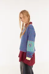 Remera de manga larga con corte boxy, confeccionada en algodón. Presenta un diseño de rayas horizontales en tonos azul y fucsia, con detalles de rayas verticales en los codos, tajos laterales y logo bordado en el pecho.