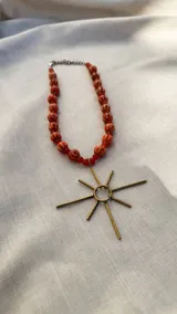 Collar con cadena de eslabones plateados y cuentas de cerámica y vidrio en color negro y gris, con dije de sol plateado. También disponible con cuentas de cerámica y vidrio en color naranja y dije de sol dorado.