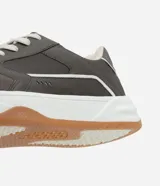 Championes urbanos de estilo street, confeccionados en material sintético color gris oscuro con detalles en blanco. Presentan cierre mediante cordones, recortes laterales decorativos y una suela de plataforma blanca con base color caramelo.