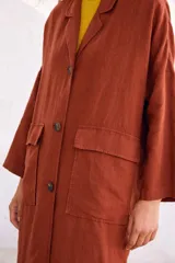 Abrigo oversize color ladrillo, confeccionado en lino pesado, con botonadura simple, bolsillos con solapa y ventilación trasera.