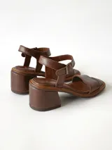 Sandalias de cuero color chocolate, con taco cuadrado de 6 cm, tira ancha en la parte delantera y tira en el tobillo con hebilla metálica ajustable.