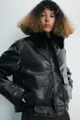 Chaqueta de efecto piel en color negro, con cuello de solapa con aplicación de pelo sintético, manga larga y bolsillos frontales de plastrón con solapa. Cierre frontal con cremallera y botones ocultos bajo solapa.