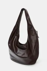 Bolso de hombro tipo saca en formato maxi, confeccionado en material sintético negro. Presenta un diseño holgado con asa integrada, cierre imantado en el compartimento principal, bolsillo lateral con cremallera y detalle de tirador.