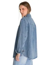 Camisa oversize de denim azul de la marca Cat, de manga larga con puños abotonados, cuello camisero y cierre frontal de botones. Presenta doble bolsillo en el pecho con etiqueta de la marca y dobladillo tipo cola de camisa.
