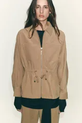 Chaqueta color tostado con cuello solapa, manga larga y cierre frontal con cremallera. Presenta bolsillos delanteros de plastrón con solapa y detalle de cintura ajustable con lazada.