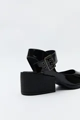 Zapato negro tipo zueco con acabado charol, tira ancha con hebilla metálica y taco ancho de altura media.