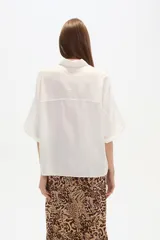 Camisa de viscosa color blanco, de corte holgado, con cuello clásico y cierre frontal de botones. Presenta mangas cortas con diseño amplio.