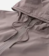 Campera rompevientos de color gris oscuro, con capucha ajustable mediante cordones, cierre frontal por cremallera y bolsillos laterales con cierre. Presenta puños elásticos y un diseño liso y minimalista.