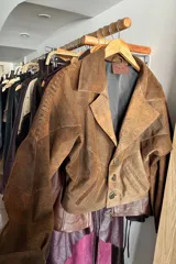 Campera bomber corta de cuero ovino en tono marrón vintage. Presenta solapas clásicas, cierre frontal con botones de guampa y detalles de pasamanería trenzada en las mangas. El interior se encuentra completamente forrado.