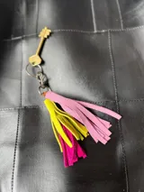 Llavero con borlas de gamuza multicolor, compuesto por un aro metálico con cierre de mosquetón y una placa metálica grabada con la marca Sierra Mora.