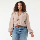 Blusa de corte fluido con estampado de cuadros vichy en tonos beige y blanco. Presenta cuello mao con cordón ajustable terminado en borlas y mangas largas abullonadas con puños elásticos.