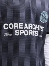 Camiseta tipo polo de manga corta con diseño de rayas verticales en tonos gris y negro. Presenta cuello polo negro, escudo deportivo en el pecho y estampa frontal con texto en color blanco. Confeccionada en tejido técnico de poliéster con corte holgado.