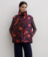 Chaleco puffer con cuello alto y cierre frontal oculto, estampado con diseño floral y de aves en tonos rojos sobre base azul oscuro.