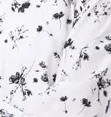 Blusa blanca de manga larga con estampado de hojas pequeñas en gris. Tiene cuello redondo, cierre frontal con botones personalizados y mangas abullonadas con puños elásticos.