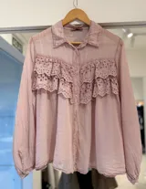 Camisa rosa de manga larga con cierre frontal de botones, cuello clásico y detalles de volados con bordado broderie en el frente.