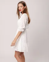 Vestido corto negro de broderie de algodón, con escote en V, mangas tres cuartos, cintura elastizada, falda corte A con volado y forro interior.