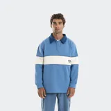 Buzo estilo rugby de manga larga con cuello camisero en contraste. Presenta un diseño de bloques de color con una franja horizontal central en tono claro y logo bordado en el pecho.