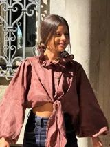 Camisa de lino color marrón, con cuello con volados, mangas largas amplias y cierre frontal con nudo ajustable.