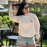 Buzo color crema de algodón con cuello redondo y mangas largas. Presenta un pequeño estampado de una lata de mermelada de frutilla en el pecho.