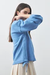 Sweater de tejido liviano con silueta relajada, hombros caídos y mangas largas con puños ajustados. Presenta cuello redondo y lazos ajustables en el bajo.