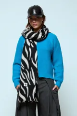 Bufanda rectangular con estampado animal print de cebra en blanco y negro, con detalle de etiqueta cuadrada con logo en el extremo inferior.