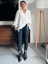 Blusa blanca de estilo romántico con volados tipo shabot en el frente, cuello alto con lazo ajustable y mangas largas abullonadas con puños ajustados.