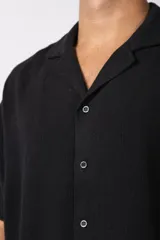 Camisa de manga corta con cuello cubano, confeccionada en lino entramado de textura natural. Presenta un corte relajado y cierre frontal con botones.