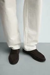 Mocasín de vestir para hombre, fabricado en piel con acabado en serraje de color azul marino. Presenta un diseño clásico con detalle de antifaz en el empeine, horma redonda, costuras visibles en el contorno y una suela sutil con ligero tacón.