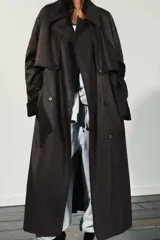 Gabardina larga de efecto encerado en color marrón oscuro, con cuello solapa y cierre frontal cruzado con botones. Presenta mangas largas con puños vueltos en pana, bolsillos laterales y cinturón ajustable de pana. Incluye pinza en la espalda.