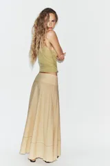 Falda larga de tiro medio en color beige, con tejido de textura cuadriculada. Presenta un diseño acampanado con detalle de costura horizontal y bajo acabado en volante. Cierre lateral con cremallera oculta.