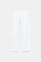 Pantalón barrel color blanco, de tiro bajo, pernera holgada que se estrecha hacia los tobillos, con bolsillos delanteros y cierre frontal con cremallera, botón interior y ganchos.