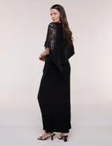 Vestido largo azul marino de seda fría, compuesto por una falda recta con tajo frontal y una capa superior superpuesta de encaje con lentejuelas bordadas, escote a la base y mangas tres cuartos acampanadas.