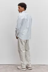 Camisa de manga larga en color celeste con estampado de rayas verticales finas, cuello abotonado y cierre frontal con botones.