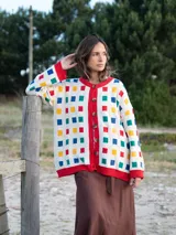Cardigan de punto color crudo con estampado de cuadrados multicolores, cuello redondo, cierre frontal con botones y terminaciones en tejido acanalado rojo.