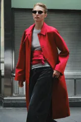 Trench largo ZARA Woman Collection de color rojo con cuello solapa, manga larga y bolsillos laterales ocultos. Presenta forro interior a contraste y cierre frontal con botones a presión.