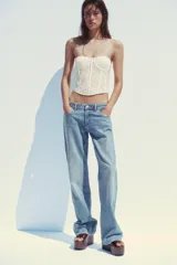 Corsé sin mangas color blanco roto, confeccionado en encaje floral, con escote recto y aros. Presenta cierre frontal con ganchos metálicos.