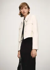 Chaqueta corta de diseño recto con cuello camisero y cierre frontal de botones ocultos. Presenta un estampado de rayas verticales finas, dos bolsillos de parche en la parte delantera y manga larga.