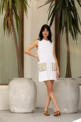 Vestido corto tejido en hilado de algodón en punto dolor, color blanco, con cuello redondo y sin mangas. Presenta dos bolsillos de lino aplicados en el frente.