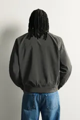 Campera bomber regular fit de tejido técnico ligero color verde oscuro, con cuello, puños y ruedo en rib elástico, bolsillos laterales de vivo y cierre frontal con cremallera.