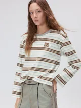 Remera de manga larga con diseño a rayas horizontales en tonos azul, blanco y negro. Presenta un cuello redondo al tono y un logo bordado en el pecho. El diseño destaca por tener un patrón de rayas diferente en las mangas y un calce holgado.