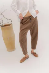 Pantalón de gabardina color marrón, con tiro bajo y calce relajado. Presenta una botonadura frontal visible como detalle principal y largo hasta el tobillo.