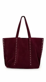 Bolso tipo shopper color bordó, confeccionado en material símil gamuza, con detalle de tachas metálicas plateadas en los laterales y en las tiras frontales. Cuenta con doble asa de hombro y cierre mediante broche.