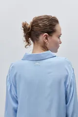 Camisa de viscosa color celeste, de calce amplio y caída fluida, con cuello clásico, cierre frontal de botones y detalles calados en mangas y delantero.